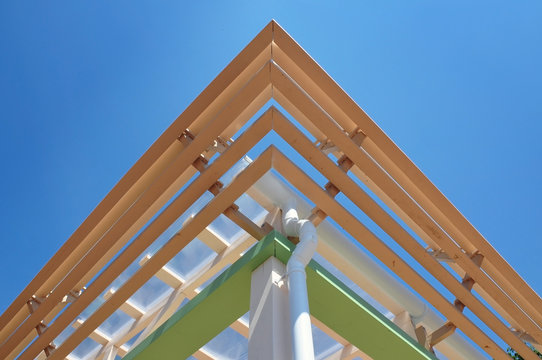 Modern roof construction. Multilevel cornice of the roof of a wooden frame with a drain pipe. Symmetrical view, look up.