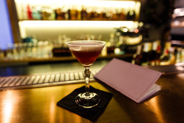 A dark image of a cocktail in a martini glass on a bar stand, menu, bokeh, small depth of field.