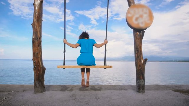 Ocean Beach in Bali. Girl. Swing. Turquoise ocean, clear sky. The girl in a blue dress on a swing. From this location offers unforgettable views, the island of Bali