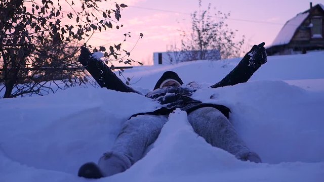 young girl lying in the snow and waving his arms and legs in different directions. SLOW MOTION