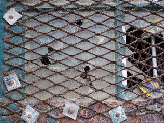 Rusty metal grid across broken window with rusty bolts and peeling rusting paint