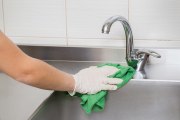 Hand in protective glove with rag cleaning kitchen equipment in the professional kitchen. Stainless steel sink. Early spring cleaning or regular clean up. - obrazy, fototapety, plakaty