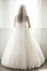 Beautiful bride in white wedding dress looking in window