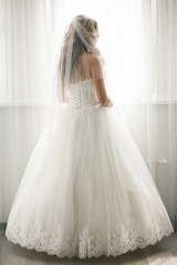 Fototapeta na wymiar Beautiful bride in white wedding dress looking in window