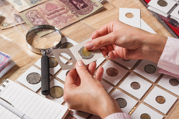 Woman looks at the collector s coin - obrazy, fototapety, plakaty