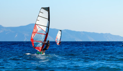 Back view of two windsurfers in action mooving parallel to each other
