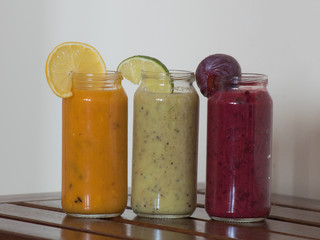 Fresh raspberry, banana, spinach and orange drinks on wooden table.
