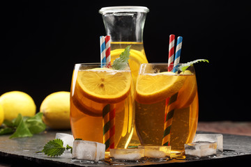 Iced tea with lemon slices, mint and ice on rustic background