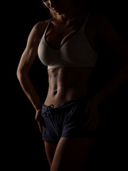 Fototapeta na wymiar Young athletic and sexy woman in a white sports shirt and blue shorts in the studio on a black background shows strong biceps and a flat belly with the perfect abdominal muscles, dark black background