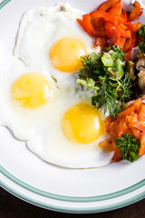 Fried eggs with mushrooms, tomatoes and basil on rustic wooden table. Natural food concept
