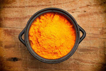 Azafrán en polvo dentro de un cuenco negro sobre tabla de madera rústica. Vista superior