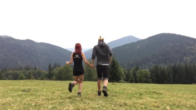 Young mand woman run on the meadow amonth the mountains and jump happily. Slow motion.