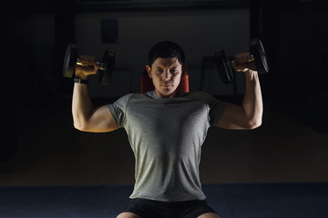Fototapeta na wymiar Muscular man training his shoulders with dumbbells.