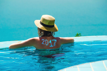 Woman from behind in hat and infinity pool looking away. New travel season concept. 2017 written on back by suncream