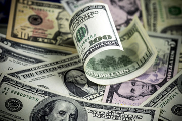 Half rolled hundred us dollar bill lying on different us dollar bills. Background. Selective focus.