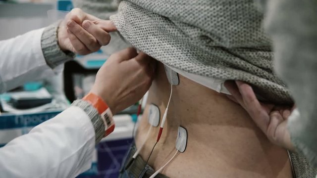 close-up nurse installs equipment on the patient's back, professional electrotherapy on man body.
