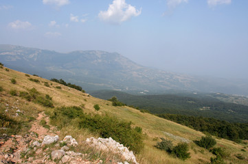Fototapeta premium The summer mountain landscape with hillside covered by dry grass and distant mountains in gauze. This photo was taken in mountainous massif Chatyr-Dag, Crimea. 