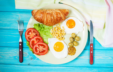 Breakfast on a wooden table. Fried eggs, tomatoes, croissant