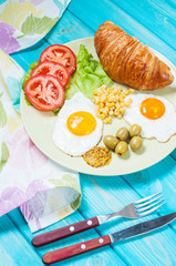 Breakfast on a wooden table. Fried eggs, tomatoes, croissant