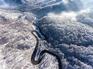 Fototapeten Aerial drone view of a curved winding road through the forest  © Calin Stan