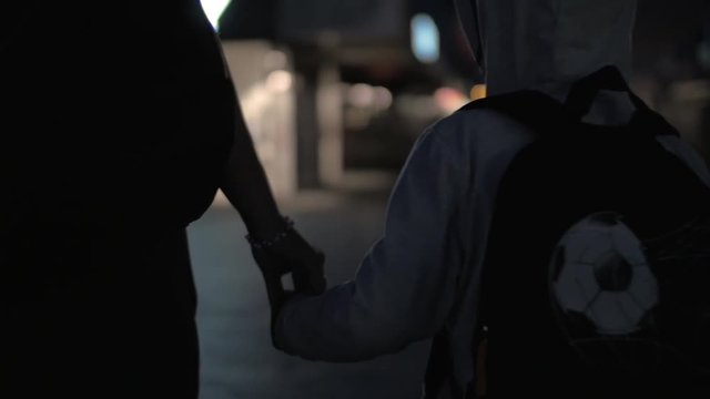 Slow motion steadicam shot of mother and son holding hands when walking in night city