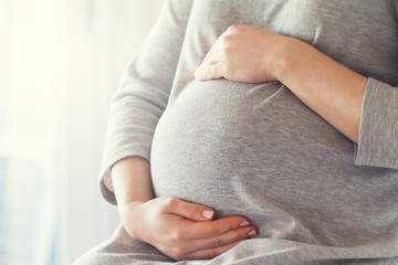 Young pregnant woman holds her hands on her swollen belly. Love