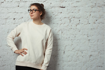 Portrait of charming woman hipster wearing blank sweater and eye glasses. White bricks wall...