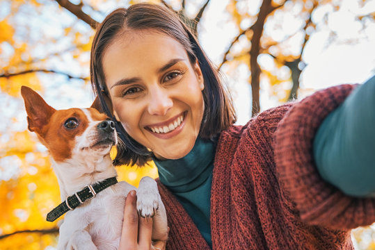 smiling young woman with dog outdoors in autumn making selfie