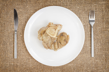 Linen background with boiled pork on plate with knife and fork