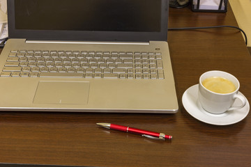 Comfortable working place in office with wooden table, laptop, ballpoint and cup of coffee.