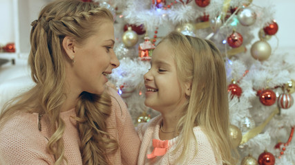 Daughter hugging and kissing her mother near Christmas tree