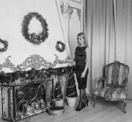 Naklejka na ściany i meble beautiful girl in black dress on Christmas evening by the fireplace, black white.