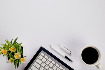 Office desk table with keyboard, notebook, pen, cup of coffee and flower. Top view with copy space (selective focus)..