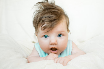 Blue-eyed baby lies on a soft blanket and looking forward.
