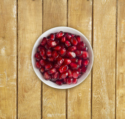 Pomegranate seeds on a wooden background. Red grains of a pomegranate in ceramic bowl. Top view.