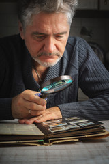 Man considers album of stamps trough the magnifying glass