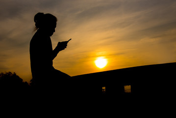 Side view of young girl using mobile phone in the sunset sky