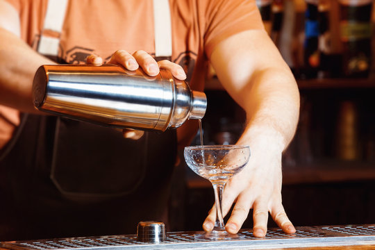 Male bartender is making cocktail pouring alcohol from shaker