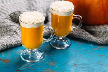 Pumpkin spiced latte or smoothie with whipped cream in glass on blue background Autumn or winter hot drink.