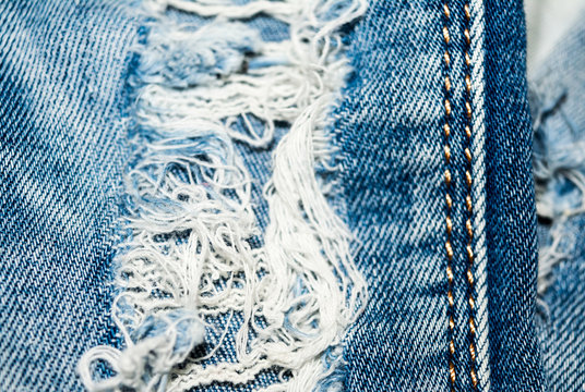 Holey jeans. Blue denim texture. Threads, seam.