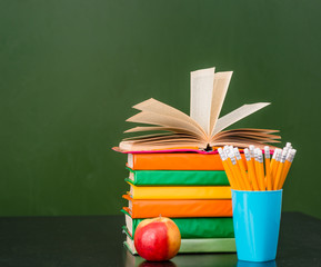 Open book on stack of books near empty green chalkboard