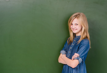 Young girl standing near empty green chalkboard. Space for text