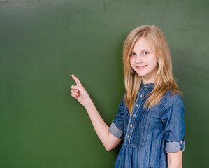 Young girl points on empty green chalkboard