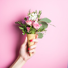 Beautiful flower in ice cream cone in girls hand with manicure on pink background