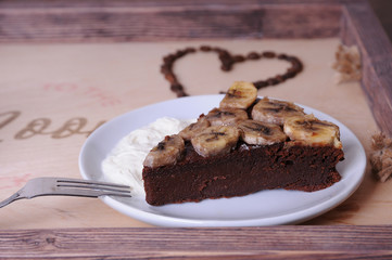 A piece of chocolate cake with banana on a white saucer. Close-up. Heart of coffee beans at the...