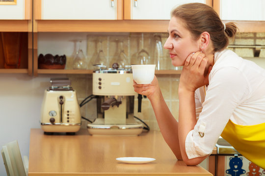 Mature woman drinking cup of coffee in kitchen.