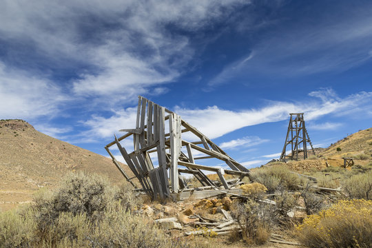 Old mining head frame in the Nevada Desert under blue sky with clouds.