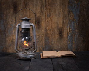 Vintage kerosene lamp and book on a wooden background