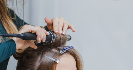 Fototapeta premium stylist making ringlets to brunette woman. Hairdresser working w