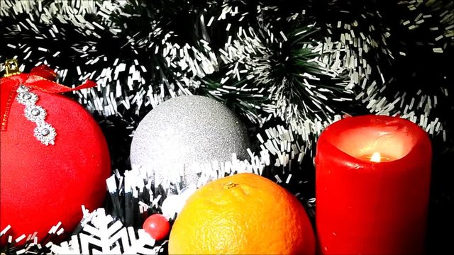 Cristmas toy, tangerine and burning candle  on background of pine-needles